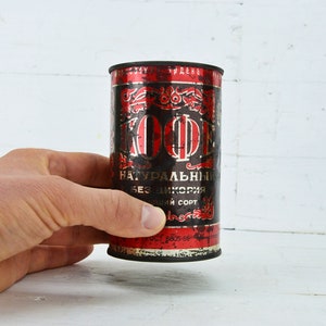 May include: A vintage metal can of coffee with red and black lettering. The can reads "KOFFE NATУРАЛЬНЫИ БЕЗ ЦИКОРИЯ ВЫСШИИ СОРТ".