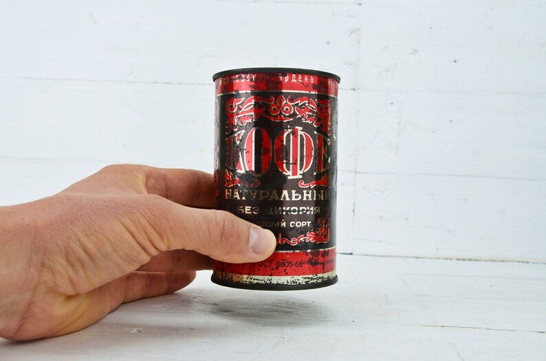 May include: A vintage metal can of coffee with red and black lettering. The can reads "KOFFE NATУРАЛЬНЫИ БЕЗ ЦИКОРИЯ ВЫСШИИ СОРТ".