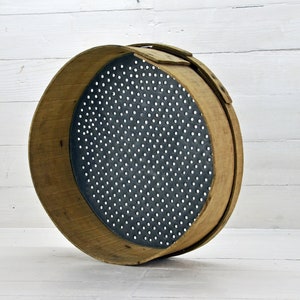 May include: A round wooden sieve with a metal mesh bottom. The sieve is made of natural wood and has a rustic look.