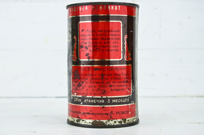 May include: A vintage metal can of coffee with red and black text. The can reads "Кофе, натуральный высшего сорта - смесь нескольких видов кофе подобранных для создания лучшего, вкуса - и аромата напитка." and "СРОК ХРАНЕНИЯ 5 МЕСЯЦЕВ".