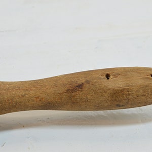 Puede incluir: Un rodillo de madera con una esponja morada unida a un extremo. El rodillo tiene dos agujeros perforados en el mango.