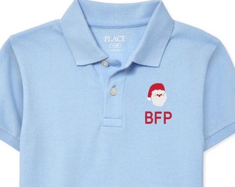 May include: Light blue polo shirt with a Santa Claus graphic and the letters "BFP" embroidered in red. The shirt has a collared neckline and short sleeves. The brand "PLACE" is visible on the collar.