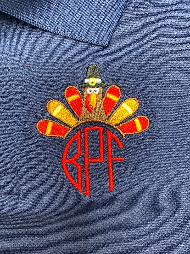 Puede incluir: Una camisa polo azul marino con un dise&ntilde;o de pavo de Acci&oacute;n de Gracias bordado. El pavo lleva un sombrero de peregrino y tiene un dise&ntilde;o de plumas rojas, amarillas y marrones. La camisa tambi&eacute;n tiene un monograma "RPF" bordado en rojo.