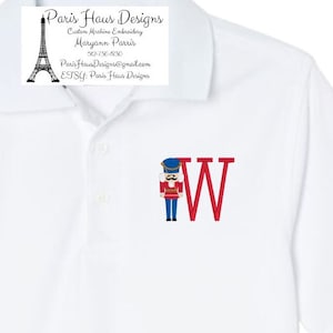 May include: White polo shirt with a red and blue embroidered nutcracker and the letter W.