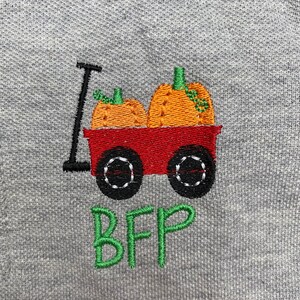 Puede incluir: Una sudadera gris con un dise&ntilde;o bordado de un carro rojo que lleva dos calabazas naranjas. El texto "BFF" est&aacute; bordado debajo del carro en verde.