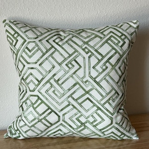 May include: A square throw pillow featuring a white fabric base with a repeating geometric pattern in shades of green. The design consists of interconnected lines and angular shapes that create a complex, maze-like motif across the entire surface.