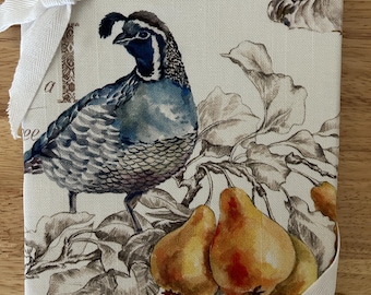 May include: A fabric-covered journal featuring a watercolor illustration of a quail, pears, and foliage. The journal is tied with a white ribbon. The color palette includes shades of blue, brown, and yellow, creating a rustic, nature-inspired design.