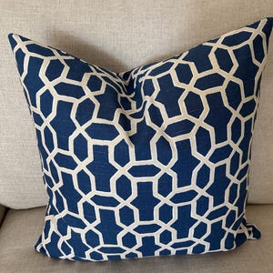 May include: A square throw pillow featuring a deep navy blue fabric base with a prominent, repeating geometric lattice pattern in a light cream color. The design consists of interconnected hexagonal and elongated shapes across the surface.