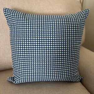 May include: A square throw pillow featuring a classic navy blue and white gingham check pattern. The fabric displays a consistent grid of small, alternating dark blue and white squares across the entire surface of the cushion cover.