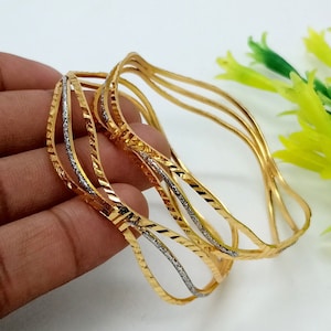 May include: Set of four gold bangles with a wavy design and a silver stripe. The bangles are stacked on top of each other.