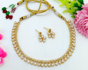 May include: A gold necklace with a delicate chain and white pearl accents. The necklace is paired with matching earrings featuring a flower design with white pearls.