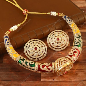 May include: A gold necklace with a colorful enamel design and a matching pair of earrings. The necklace is made of metal and has a round pendant with a red stone in the center. The earrings are also round and have a red stone in the center.