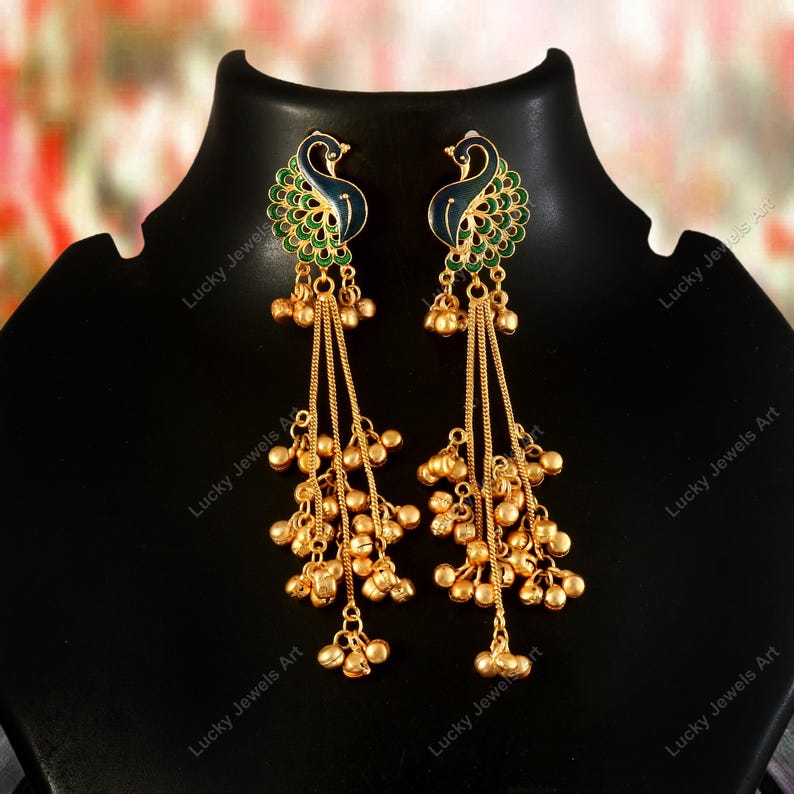 May include: A pair of gold-colored earrings with a peacock design. The earrings feature a peacock head with blue and green enamel detailing. Long chains with small gold beads hang from the peacock design.