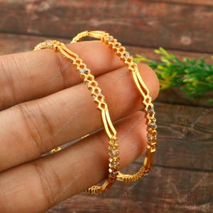 May include: Two gold bangles with a diamond-like pattern. The bangles are stacked on top of each other.