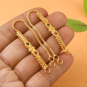 Puede incluir: Cadenas doradas para pendientes con detalles decorativos en forma de estrella. Cada cadena presenta una serie de pequeñas cuentas redondas y está adornada con piedras preciosas rojas y negras. Las cadenas están diseñadas para sujetarse a los pendientes.