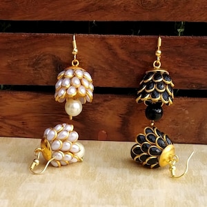 May include: A pair of dangle earrings with gold-tone metal and pearl and black beads. The earrings feature a round, layered design with a pearl or black bead at the bottom.