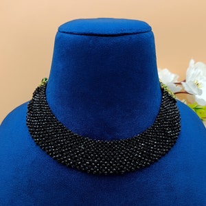 May include: A black beaded choker necklace with a layered design. The necklace is displayed on a blue velvet mannequin bust.