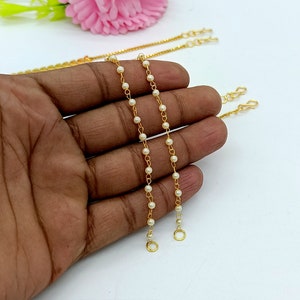 Op de afbeelding: Twee gouden kettingen met witte parels. Elke ketting heeft aan elk uiteinde een sluiting.