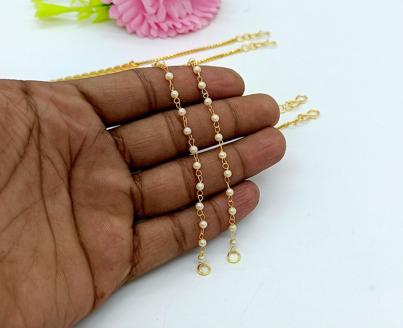 Op de afbeelding: Twee gouden kettingen met witte parels. Elke ketting heeft aan elk uiteinde een sluiting.