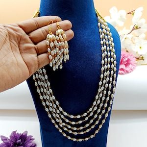May include: A multi-strand pearl necklace and matching earrings. The necklace is made of five strands of small, white oval pearls connected by gold chain links. The earrings are dangle earrings with a similar design.
