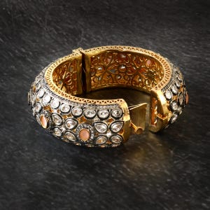 Peut inclure: Un bracelet jonc en or avec des détails complexes et des pierres précieuses blanches et roses. Le bracelet a un fermoir à charnière.