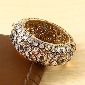 May include: A gold bangle bracelet with intricate detailing and a design of small white and blue gemstones.