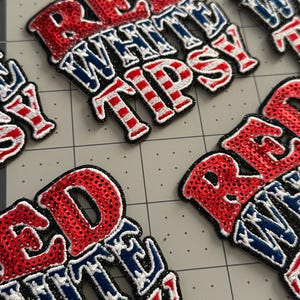 May include: Multiple embroidered patches featuring the text RED WHITE TIPSY in a stacked layout. The word RED is covered in red sequins, while WHITE and TIPSY feature a blue and white star and stripe pattern with a thick black border outline.