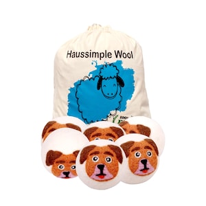 May include: A canvas bag with the text "Haussimple Wool" and a blue sheep graphic. Six white and brown dog-faced wool dryer balls are in front of the bag. The dryer balls have brown ears and noses.