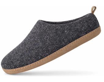 Puede incluir: Una zapatilla de fieltro gris carbón oscuro con una parte superior texturizada similar a la lana, una suela de goma color canela con costuras visibles y una pequeña lengüeta del mismo color en el talón. Tiene punta redondeada y diseño sin cordones.