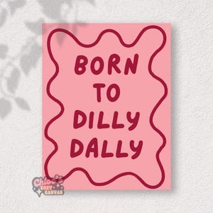 Puede incluir: Un lienzo rosa con la frase "BORN TO DILLY DALLY" en letras granates. El texto está dentro de una forma granate con bordes ondulados. En la esquina inferior izquierda aparece el texto "Chloe's Cozy + Canvas".