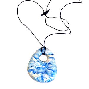 May include: A pendant necklace with a blue and white marbled stone pendant and a black cord. The pendant has an irregular shape with a hole near the top. The cord is tied in a heart shape.