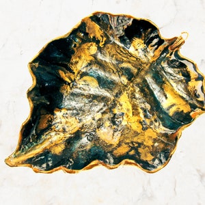 One more angle of a black and gold leaf-shaped decorative paper clay bowl-ornament with wavy edge and glossy finish. Suitable for holding keys, jewelry and other trinkets. Can be used as table, shelf décor.