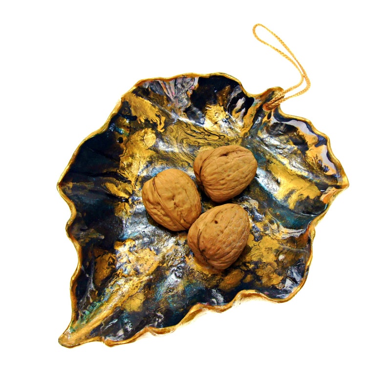 One more angle of a black and gold leaf-shaped decorative paper clay bowl-ornament with wavy edge and glossy finish. The bowl holds 3 walnuts to show its space.