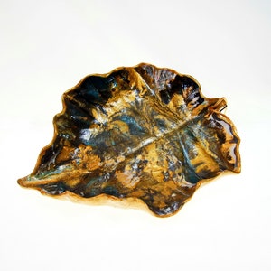 A black and gold leaf-shaped decorative paper clay bowl-ornament with wavy edge and glossy finish. Suitable for holding keys, jewelry and other trinkets.