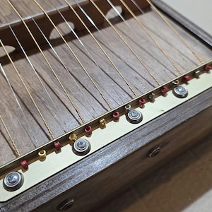 May include: A wooden musical instrument with strings and tuning pegs. The instrument has a dark brown finish and is made of wood. The strings are made of metal and are attached to the instrument with tuning pegs. The tuning pegs are made of metal and are located on the side of the instrument.