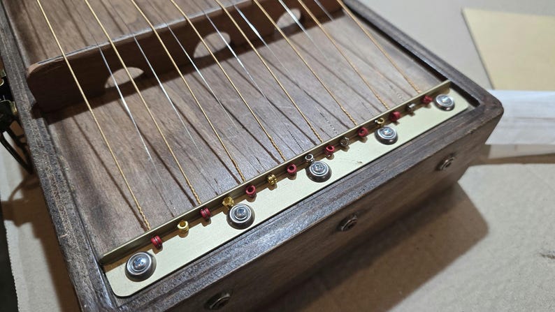 May include: A wooden musical instrument with strings and tuning pegs. The instrument has a dark brown finish and is made of wood. The strings are made of metal and are attached to the instrument with tuning pegs. The tuning pegs are made of metal and are located on the side of the instrument.