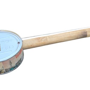 Könnte beinhalten: Ein Holzstab mit einer Metalldose an einem Ende. Die Dose hat ein Loch oben und einen kleinen Metallknopf. Der Stab hat eine Saite daran und einen Stimmwirbel am anderen Ende. Dies ist ein selbstgebautes Musikinstrument.