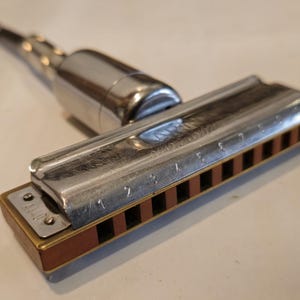 May include: A silver harmonica with a brown wooden mouthpiece and a silver metal attachment. The harmonica has numbers 1 through 7 printed on the top.