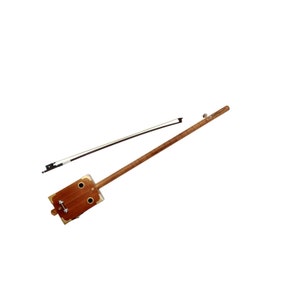 Peut inclure: Une guitare en boîte à cigares en bois avec un corps en bois brun et une seule corde. La guitare est accompagnée d'un archet noir.