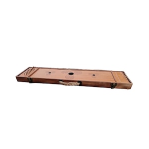 Op de afbeelding: Een houten muziekinstrument met een touwhandvat en een reeks metalen pinnen aan het ene uiteinde. Het instrument heeft een decoratief ontwerp met een rond gat in het midden.