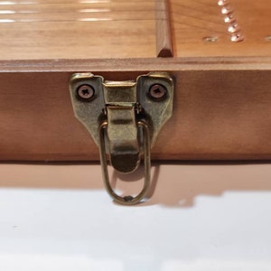 May include: A close-up of a wooden box with a brass latch. The latch has a loop handle and is secured with two screws.