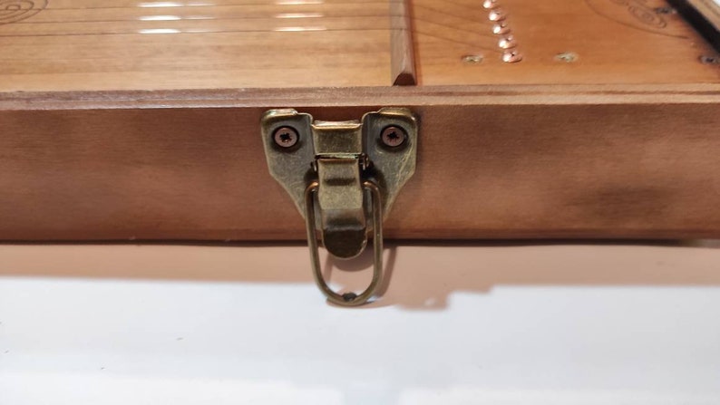 May include: A close-up of a wooden box with a brass latch. The latch has a loop handle and is secured with two screws.
