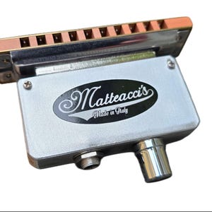 May include: A silver harmonica microphone with a copper-coloured top and a black label that reads "Matteacci's Made in Italy".