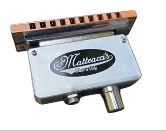 May include: A silver harmonica microphone with a copper-colored top and a black label that reads "Matteacci's Made in Italy".