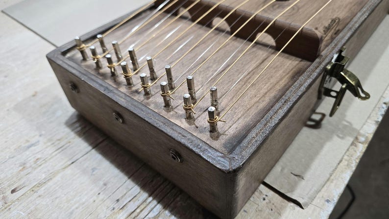 May include: A wooden musical instrument with strings and tuning pegs. The instrument has a dark brown finish and is made of wood.