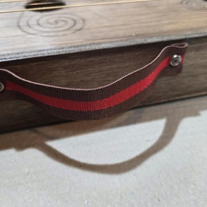 May include: A wooden box with a red and brown fabric handle. The handle has two metal rivets.