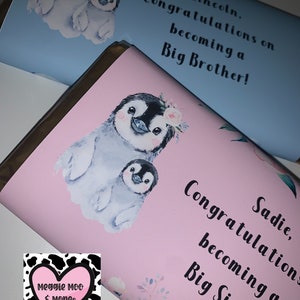 May include: Two pink and blue chocolate bar wrappers with penguin illustrations. The pink wrapper says "Sadie, Congratulations becoming a Big Sister!" and the blue wrapper says "Lincoln, Congratulations on becoming a Big Brother!"