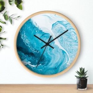 May include: A round wooden wall clock with a blue and white abstract design. The clock face has black hands and a white background.