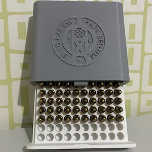 May include: A gray 3D-printed ammunition storage box with a white tray filled with brass-colored bullets. The box lid features a circular emblem with the Latin phrase "Si Vis Pacem Para Bellum."