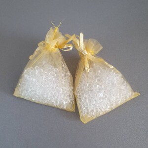 May include: Two small yellow mesh bags filled with clear silica gel beads. The bags are tied with a ribbon.